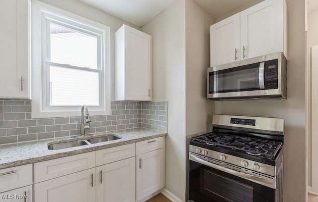 kitchen featuring appliances with stainless steel finishes, light stone counters, white cabinetry, sink, and tasteful backsplash