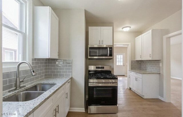 kitchen with stainless steel appliances, sink, white cabinets, and light hardwood / wood-style floors