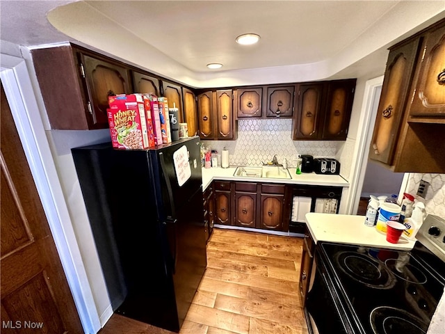 kitchen featuring tasteful backsplash, dark brown cabinetry, sink, black appliances, and light hardwood / wood-style floors