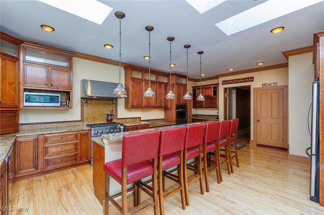 kitchen with stainless steel appliances, light hardwood / wood-style floors, wall chimney range hood, and a skylight