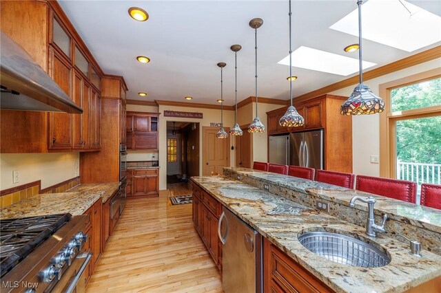 kitchen featuring appliances with stainless steel finishes, light hardwood / wood-style floors, wall chimney exhaust hood, a skylight, and light stone counters