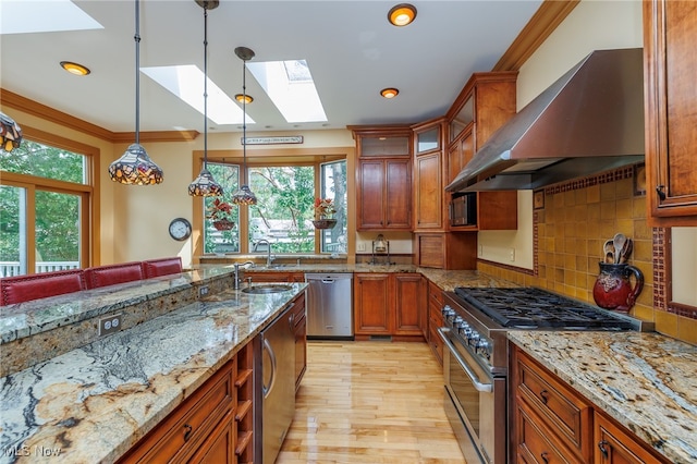 kitchen with a wealth of natural light, stainless steel appliances, a skylight, and wall chimney range hood