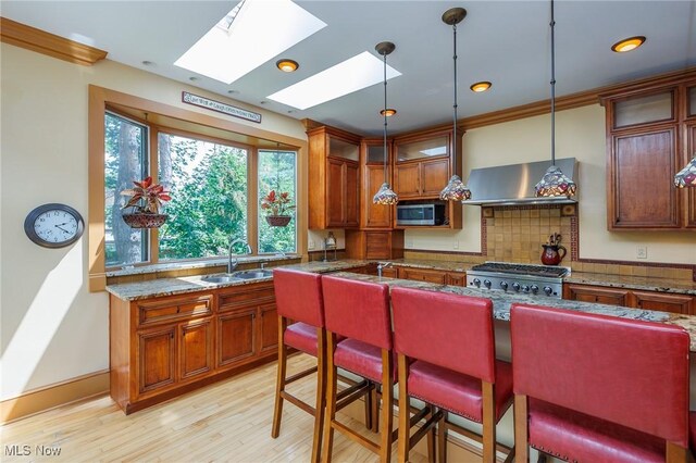 kitchen with a skylight, tasteful backsplash, sink, stainless steel microwave, and dark stone counters