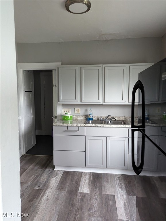 kitchen featuring sink, white cabinets, dark hardwood / wood-style flooring, light stone countertops, and black refrigerator