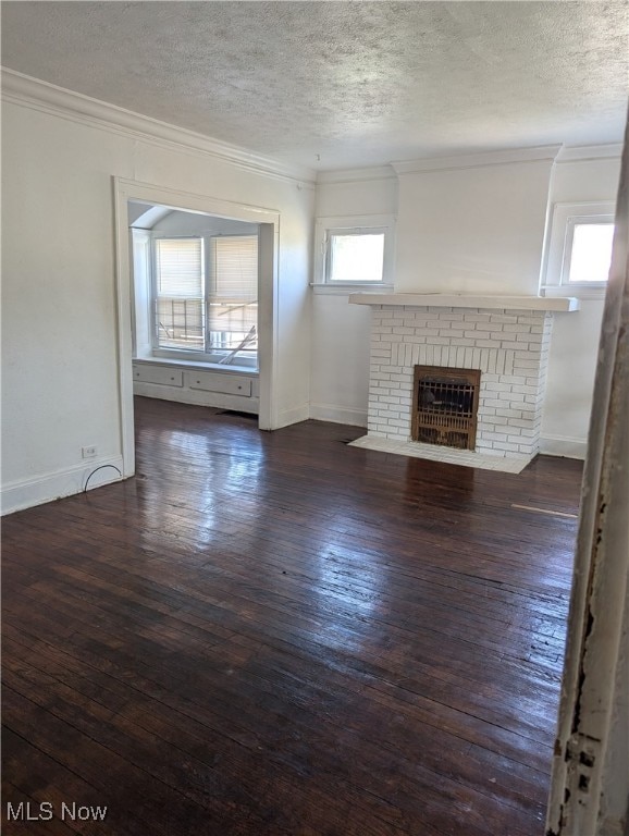 unfurnished living room featuring a brick fireplace, ornamental molding, a textured ceiling, and dark hardwood / wood-style flooring