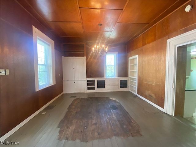 spare room featuring plenty of natural light, wood walls, and a notable chandelier