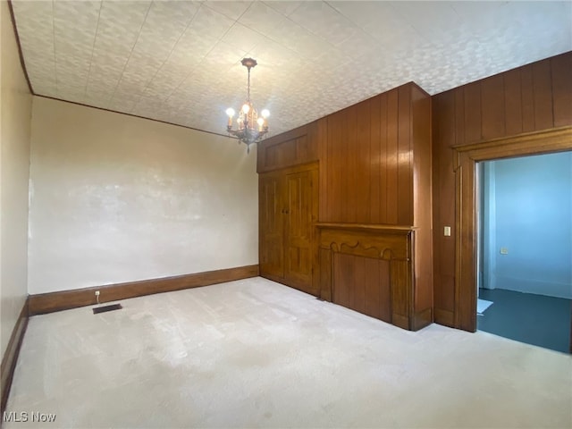 carpeted empty room with a chandelier and wooden walls