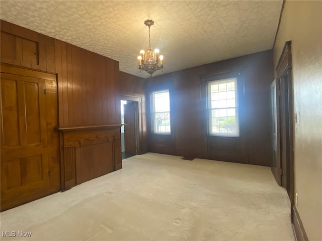 carpeted spare room with wood walls and a chandelier