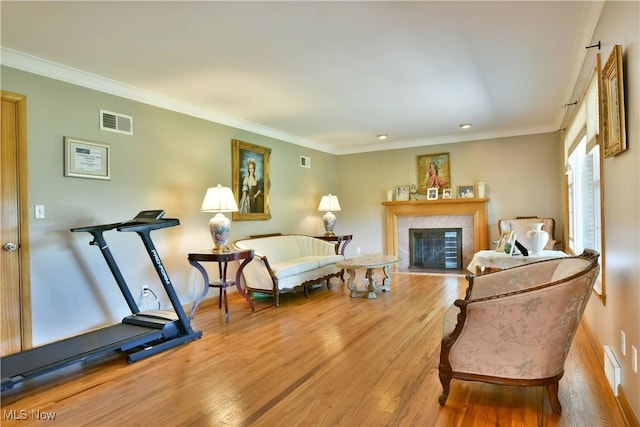 bedroom with a tiled fireplace, wood finished floors, visible vents, and crown molding