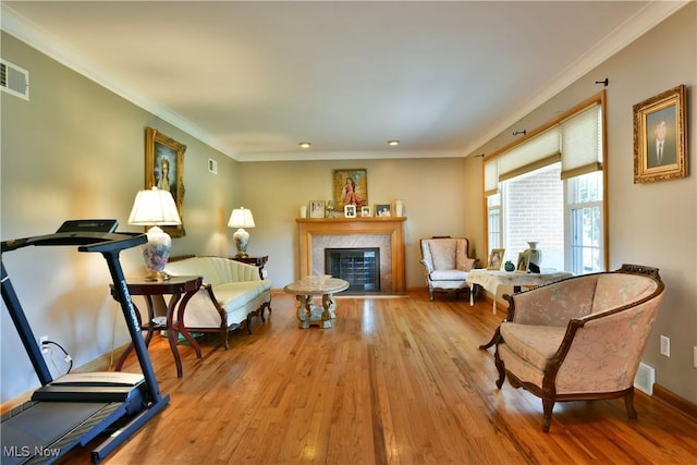 sitting room featuring light wood-style flooring, a fireplace, visible vents, baseboards, and crown molding