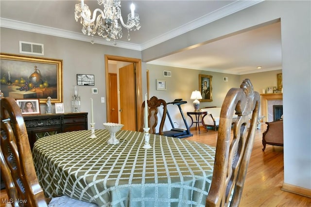 dining room with crown molding, light wood-style floors, visible vents, and a fireplace