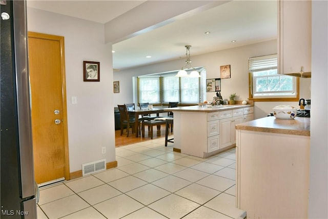 kitchen with a breakfast bar area, a peninsula, light countertops, freestanding refrigerator, and decorative light fixtures