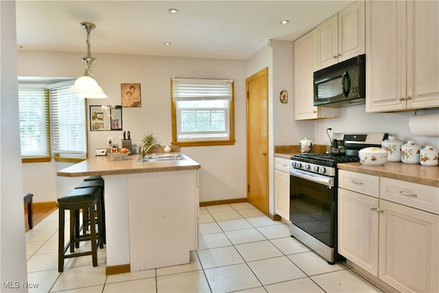 kitchen featuring light tile patterned flooring, a kitchen bar, sink, decorative light fixtures, and stainless steel range with gas cooktop