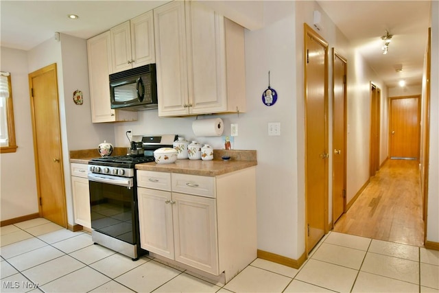 kitchen featuring light countertops, light tile patterned flooring, black microwave, stainless steel gas range oven, and baseboards