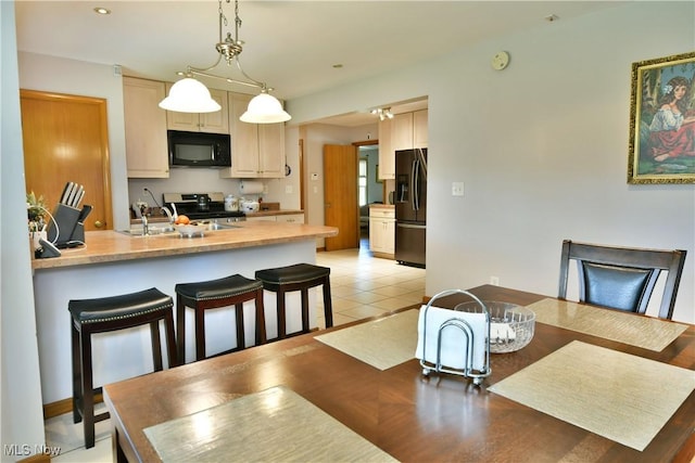 kitchen featuring light tile patterned floors, light countertops, light brown cabinetry, black appliances, and pendant lighting