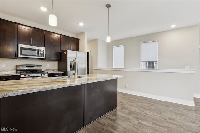 kitchen featuring stainless steel appliances, light stone counters, hardwood / wood-style flooring, and hanging light fixtures