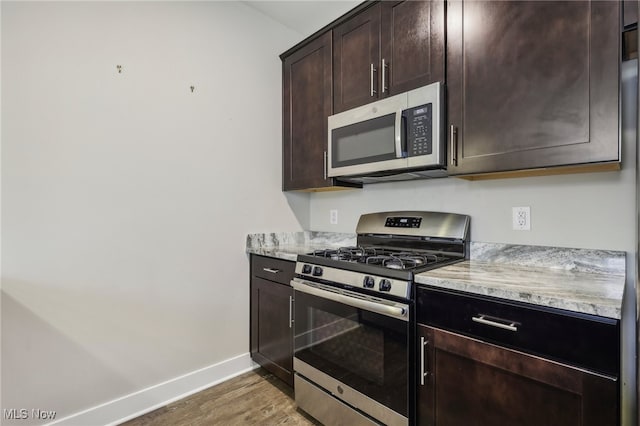 kitchen with hardwood / wood-style flooring, light stone counters, dark brown cabinetry, and stainless steel appliances