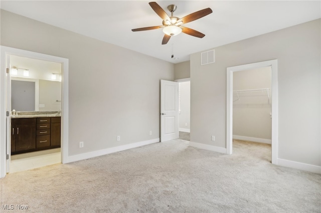 unfurnished bedroom with light colored carpet, a spacious closet, a closet, ceiling fan, and connected bathroom