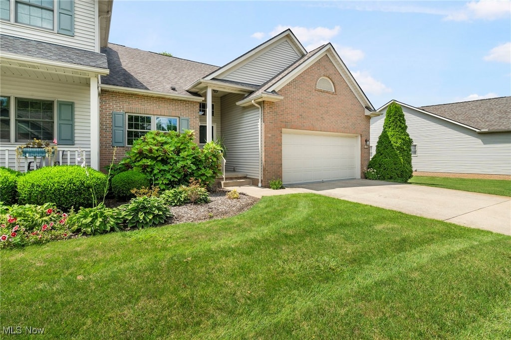 view of front facade featuring driveway, a garage, a shingled roof, brick siding, and a front yard