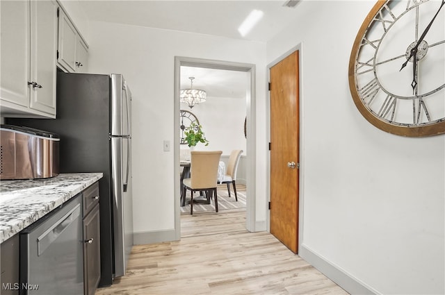 kitchen featuring light stone counters, an inviting chandelier, light wood-type flooring, and stainless steel dishwasher