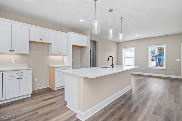 kitchen with white cabinets, sink, hanging light fixtures, a kitchen island with sink, and wood-type flooring