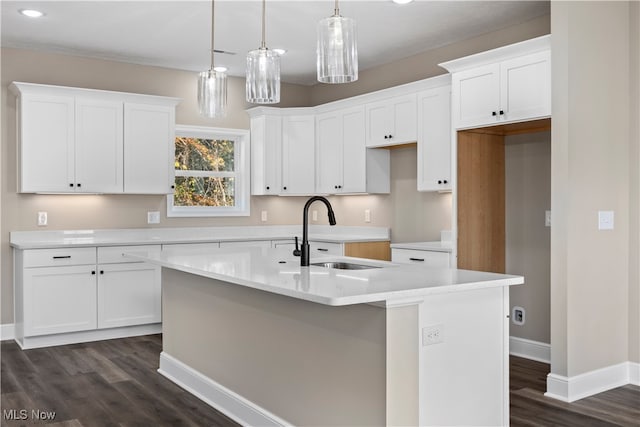 kitchen featuring dark wood-type flooring, sink, pendant lighting, white cabinetry, and an island with sink