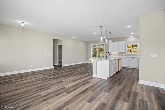 kitchen with white cabinetry, sink, dark wood-type flooring, pendant lighting, and a kitchen island with sink