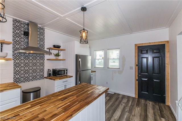 kitchen with appliances with stainless steel finishes, butcher block counters, pendant lighting, wall chimney range hood, and dark hardwood / wood-style flooring