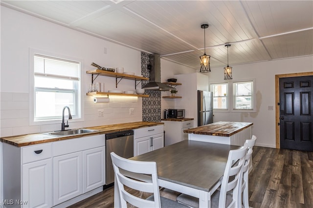 kitchen featuring wall chimney range hood, backsplash, wood counters, appliances with stainless steel finishes, and sink