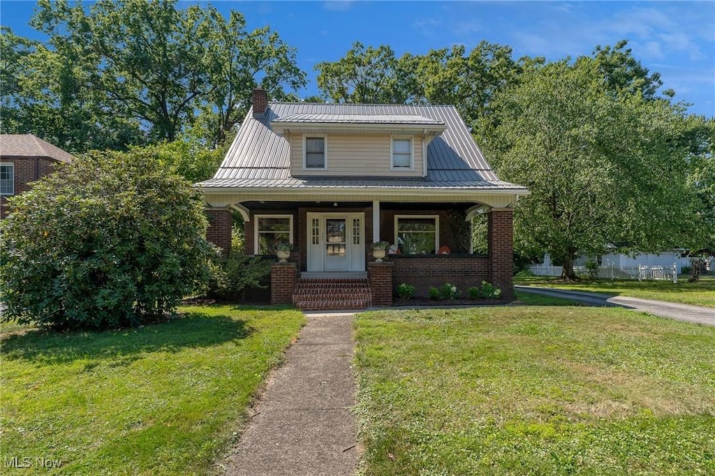 view of front of house with covered porch, metal roof, brick siding, and a front lawn