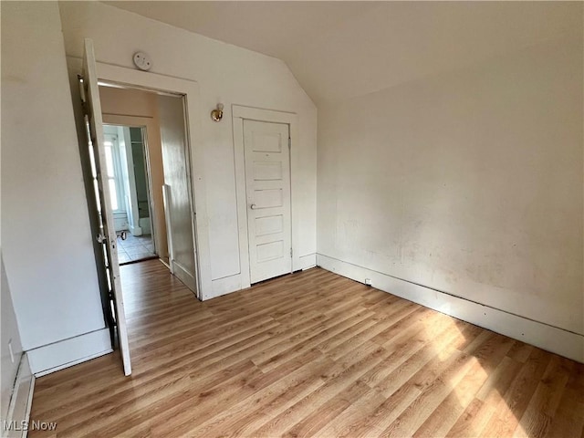 unfurnished bedroom featuring vaulted ceiling, a closet, and light wood-type flooring