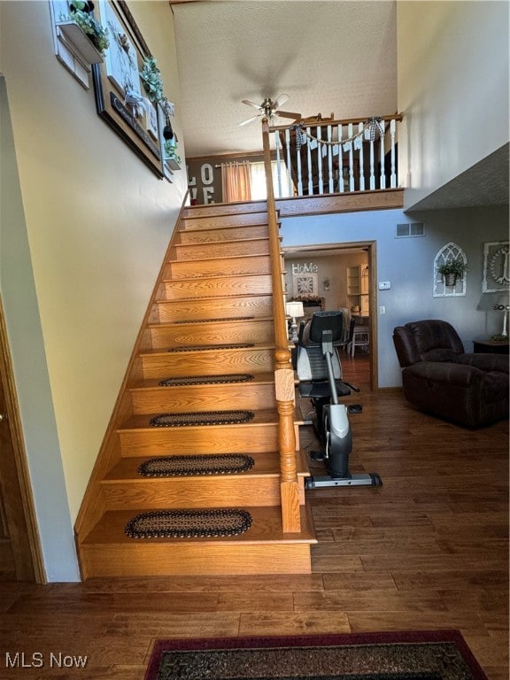 stairs featuring a textured ceiling, wood-type flooring, a high ceiling, and ceiling fan