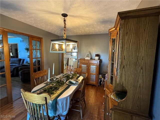 dining space featuring dark wood-type flooring, a textured ceiling, french doors, and an inviting chandelier