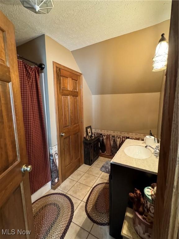 bathroom featuring a textured ceiling, vanity, vaulted ceiling, walk in shower, and tile patterned flooring