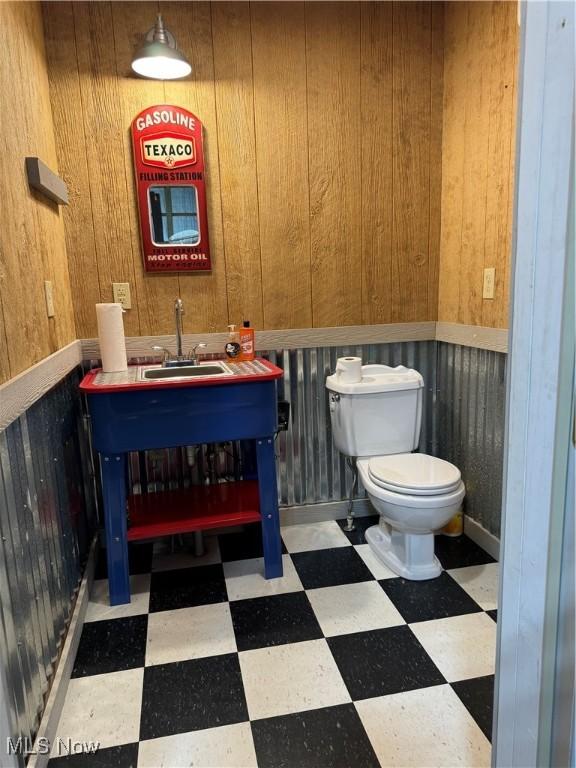 bathroom with toilet, wood walls, and sink