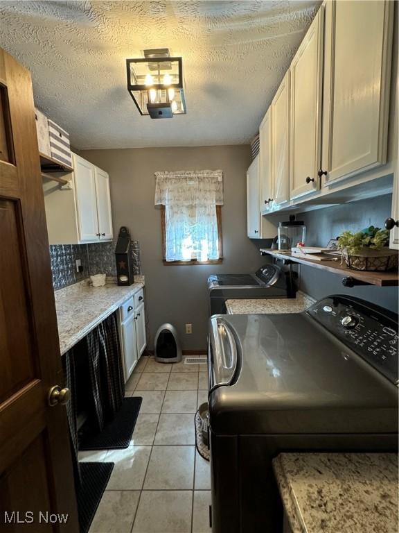 laundry area featuring a textured ceiling, cabinets, independent washer and dryer, and light tile patterned flooring