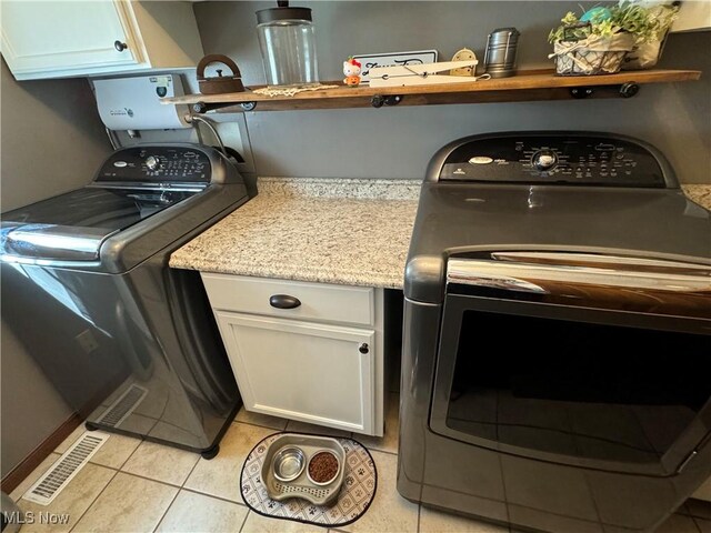 laundry area featuring washing machine and dryer, cabinets, and light tile patterned floors