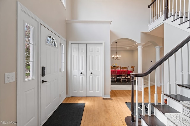 foyer entrance with a notable chandelier, a high ceiling, light hardwood / wood-style flooring, and decorative columns