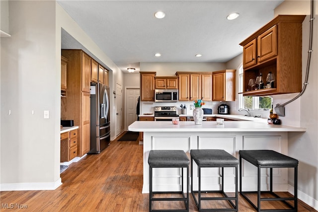 kitchen with hardwood / wood-style flooring, kitchen peninsula, a kitchen bar, and stainless steel appliances