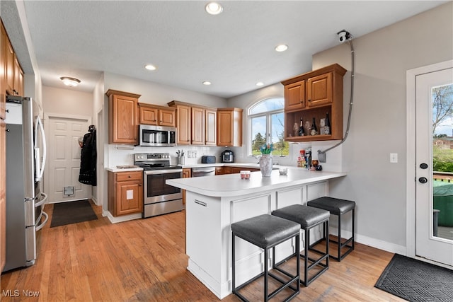 kitchen with light wood-type flooring, appliances with stainless steel finishes, kitchen peninsula, and a breakfast bar