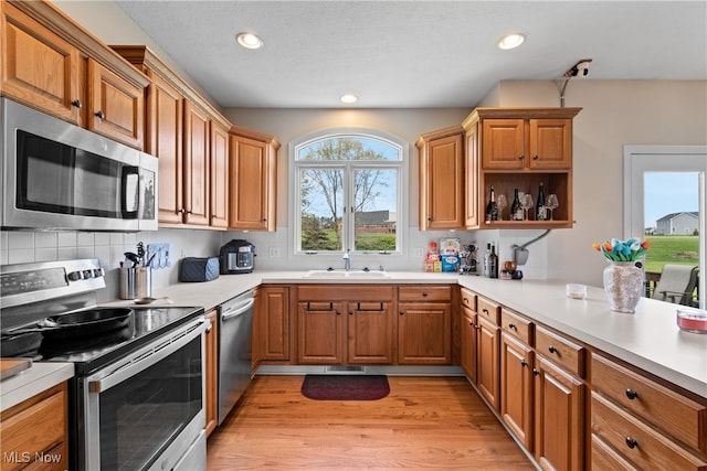 kitchen with light wood-type flooring, appliances with stainless steel finishes, sink, and decorative backsplash