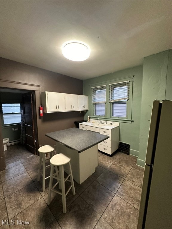 kitchen with stainless steel fridge, white cabinetry, dark tile patterned floors, and a healthy amount of sunlight