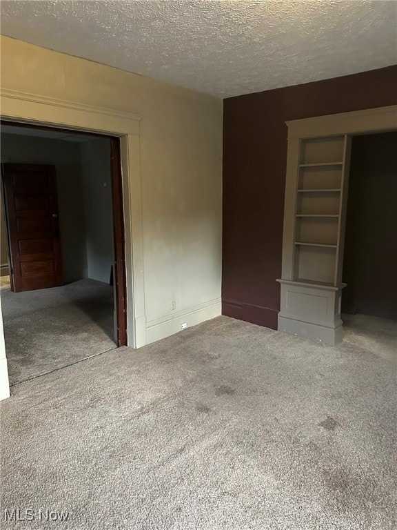 unfurnished room featuring built in shelves, a textured ceiling, and carpet floors