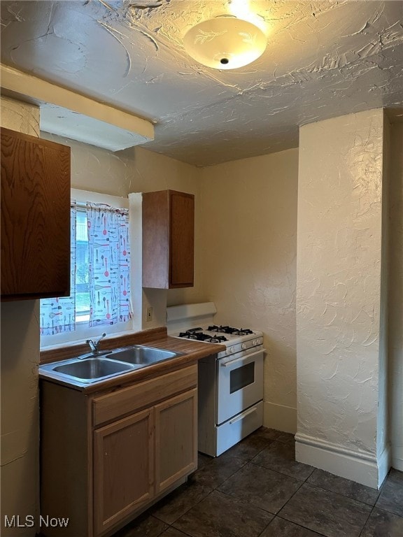 kitchen featuring sink, white gas range oven, and dark tile patterned flooring