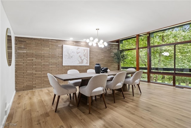 dining space with brick wall, a chandelier, expansive windows, and light wood-type flooring