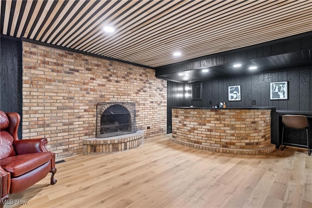 living room with a fireplace, wood walls, light hardwood / wood-style floors, and brick wall