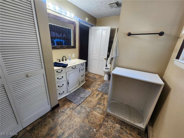 bathroom with a textured ceiling, vanity, visible vents, a closet, and stone finish floor