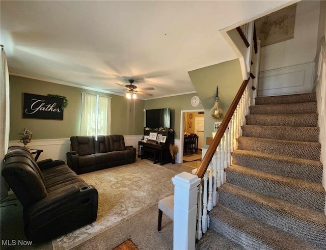 carpeted living area with ceiling fan, a decorative wall, ornamental molding, stairway, and wainscoting