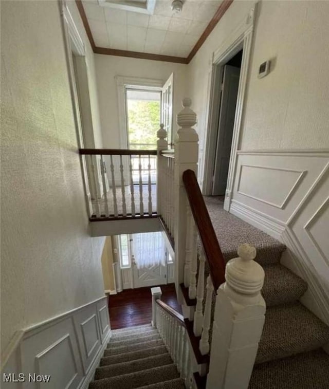 staircase featuring crown molding, a healthy amount of sunlight, wainscoting, and a decorative wall