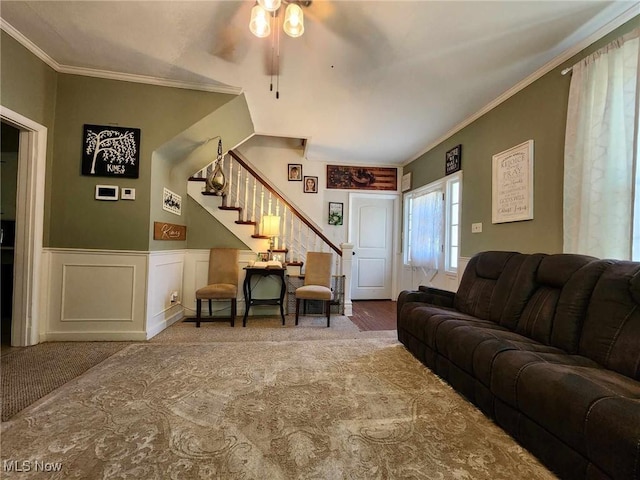 living room featuring stairs, a decorative wall, crown molding, and wainscoting